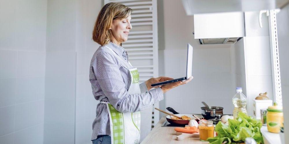 Woman wearing an apron following a recipe on her laptop computer.